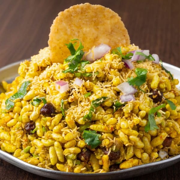 Indian bhel puri snack topped with sev, onions, cilantro, and chutney, served in a metal bowl with a crisp papdi.