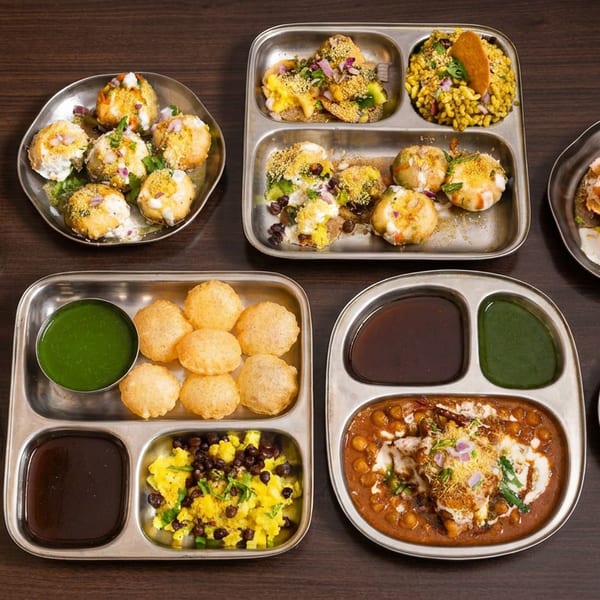 Assorted Indian street foods including chaat, pani puri, crispy snacks, and green and tamarind chutneys on metal plates.
